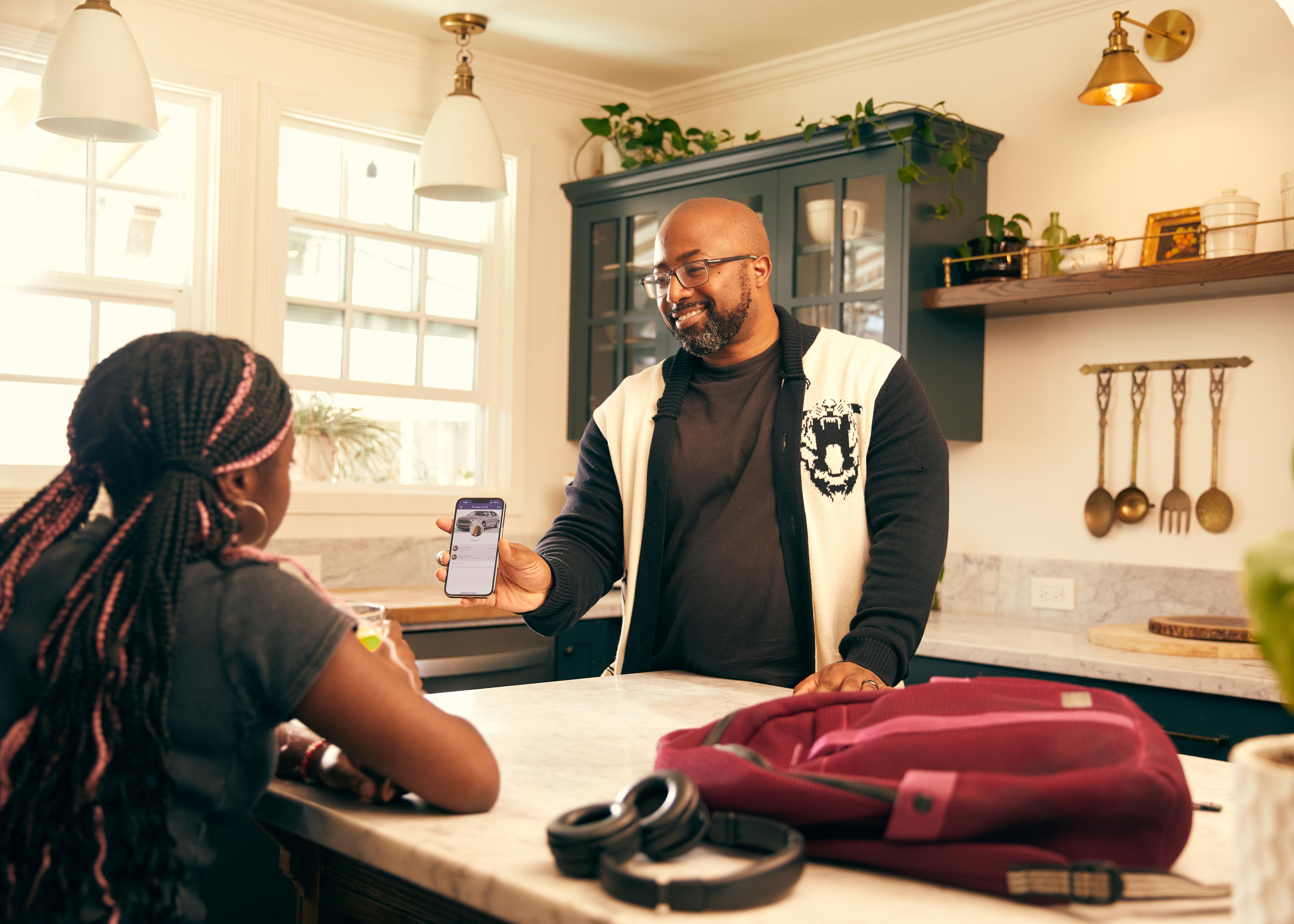 Adult and teenager having a conversation in a modern kitchen while looking at a smartphone, with backpack and headphones on counter