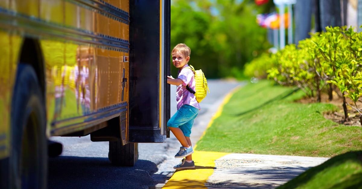 Young student with bright yellow backpack stepping onto a school bus on a sunny morning