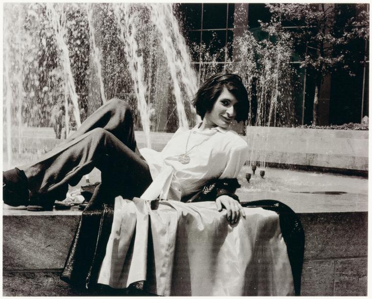 Black and white photograph of a person relaxing by a fountain, wearing casual 1970s attire