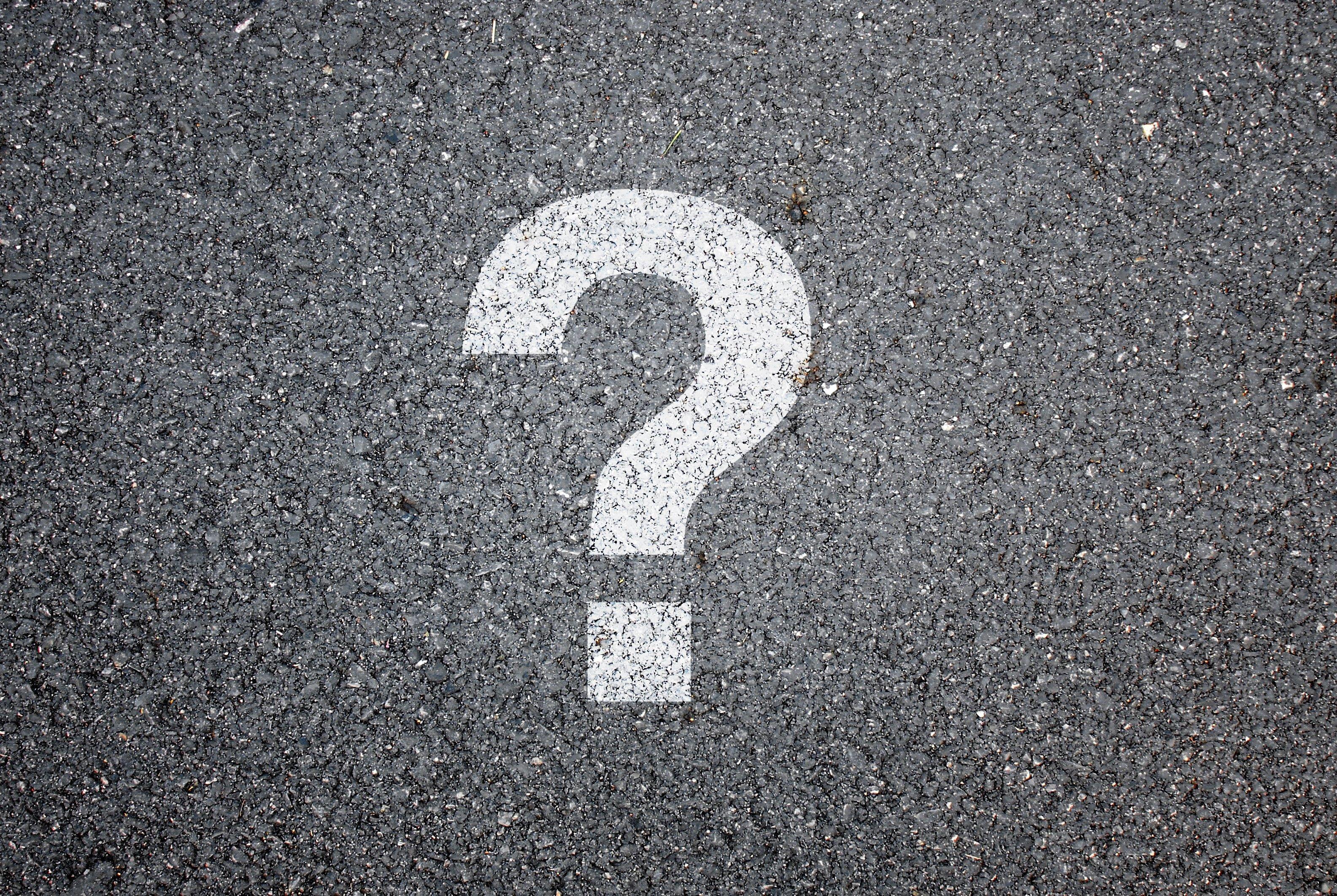 A white painted question mark symbol on dark asphalt pavement
