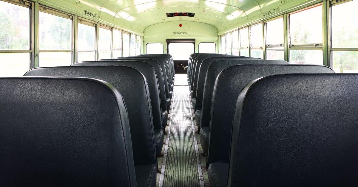 Interior view of an empty school bus showing rows of black vinyl seats and center aisle leading to the emergency exit door