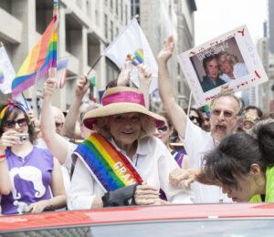 Celebratory crowd at Pride parade with rainbow flags, signs, and participants showing joyful support and solidarity