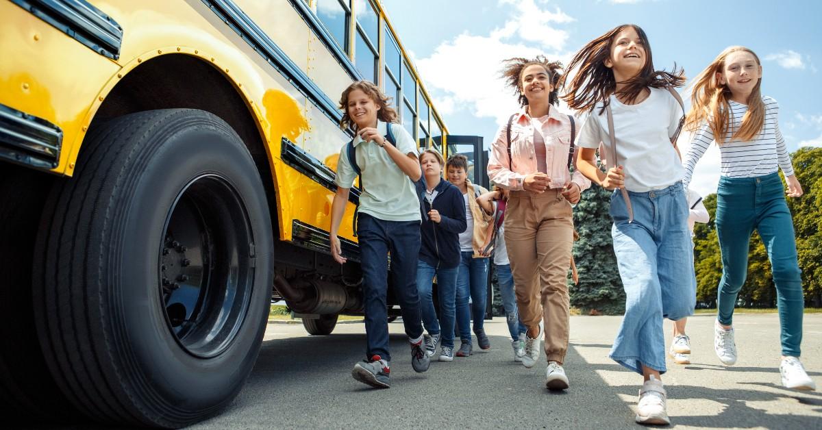 Group of middle school students excitedly walking away from a yellow school bus on a sunny day