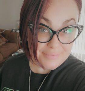 Close-up portrait of person wearing stylish cat-eye glasses and black top, with a warm smile and natural lighting