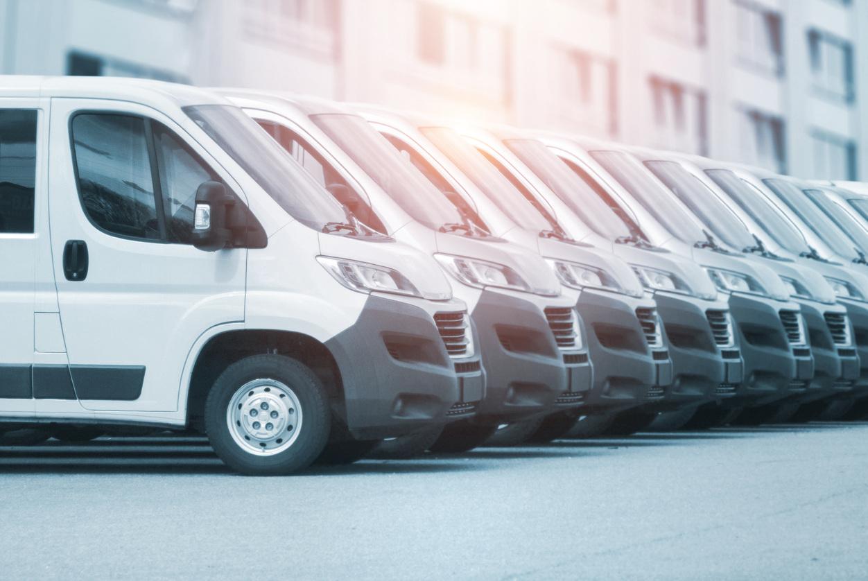 Row of identical white commercial delivery vans parked in line outside a building