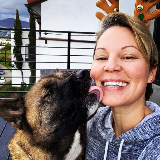 Joyful holiday moment with German Shepherd dog giving kiss while wearing reindeer antlers headband on balcony